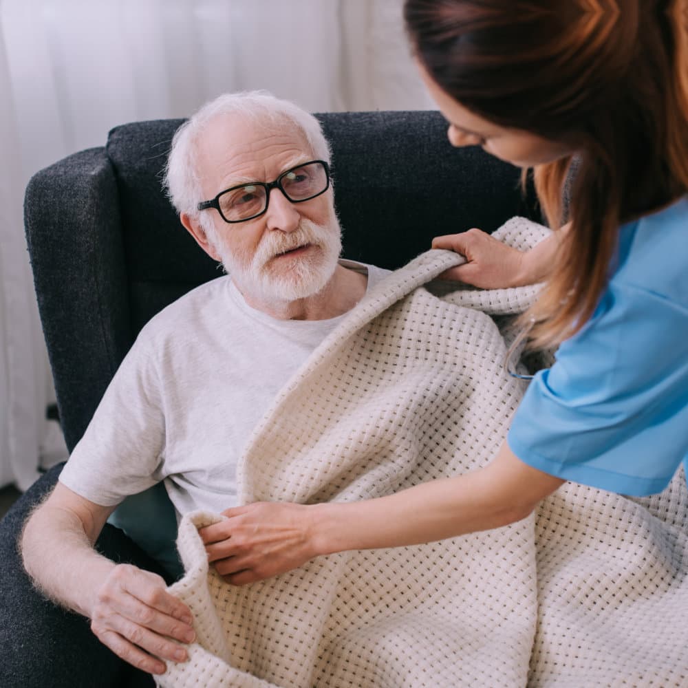 caregiver putting blanket to senior